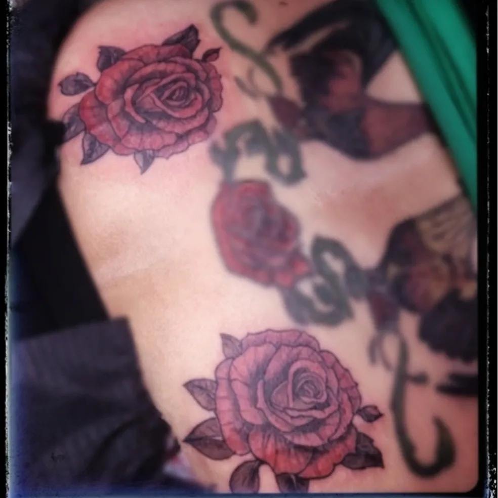 Tres rosas rojas y moradas tatuadas en el brazo