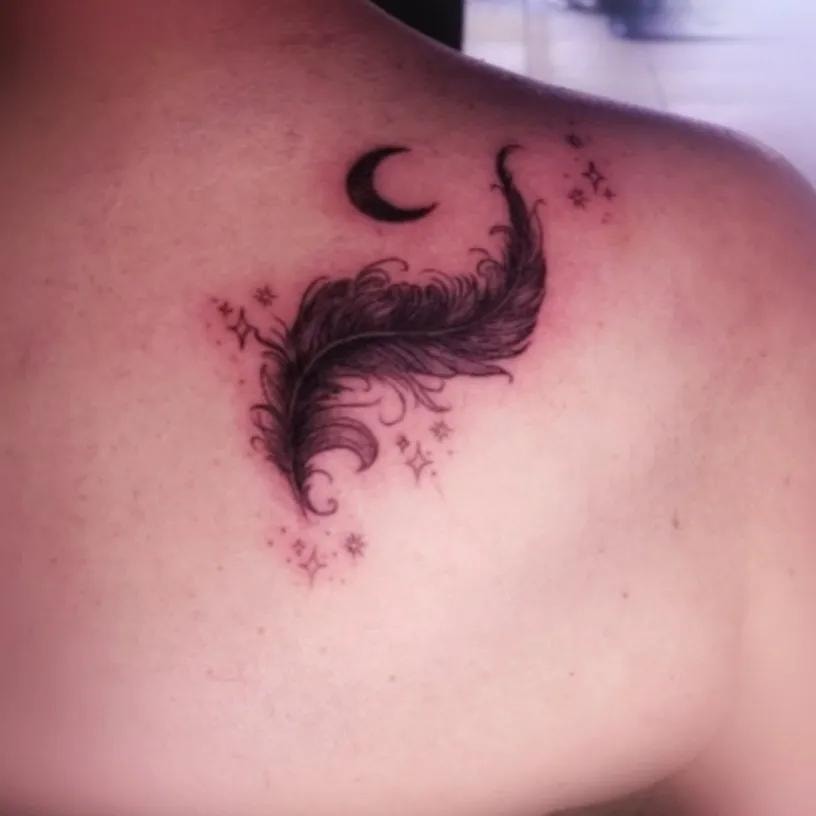 Pluma con luna y estrellas tatuada en el hombro